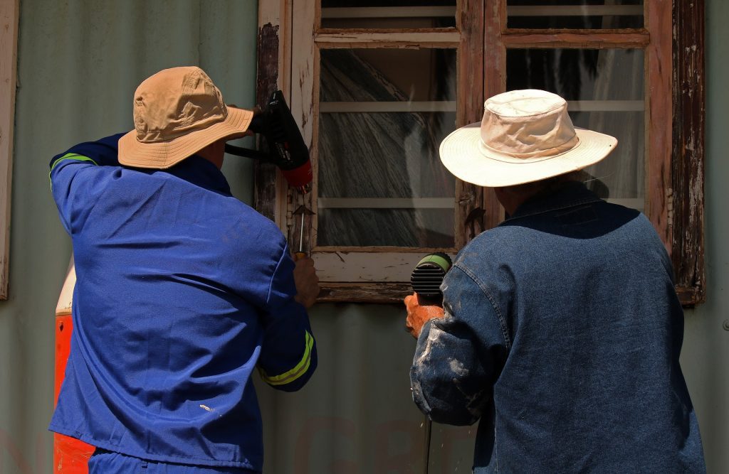men paint stripping a window